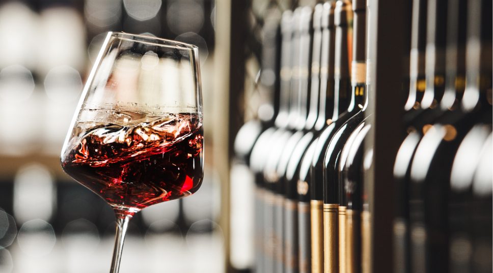Copa de vino tinto ante una estantería de botellas